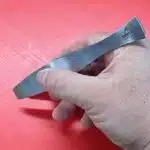 Graetenpinzette aus Edelstahl in der Hand auf rotem Schneidbrett